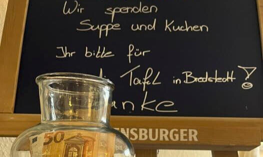 Glasflasche mit gesammeltem Geld vor Tafel mit Spendenaufruf